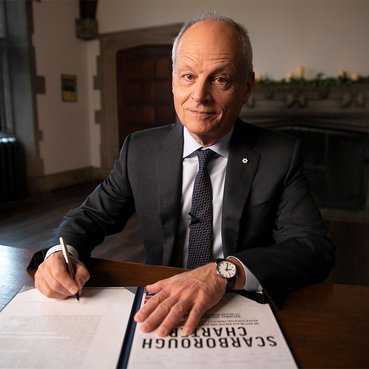 U of T President Meric Gertler sits at a desk signing the Scarborough Charter 