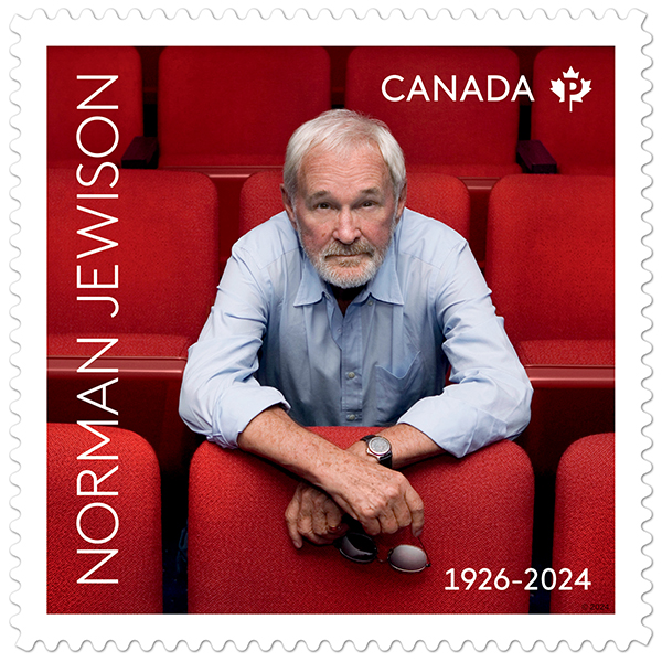 A man with white hair and a white goatee beard sits among theatre seats.