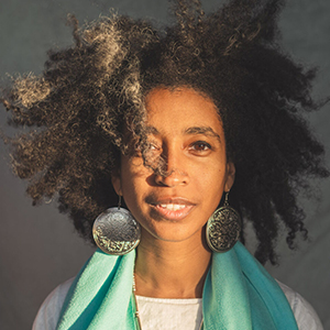 A woman with curly brown hair and a turquoise scarf smiles at the camera