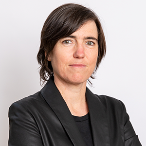 A woman with dark hair, black top and black jacket looks at the camera.
